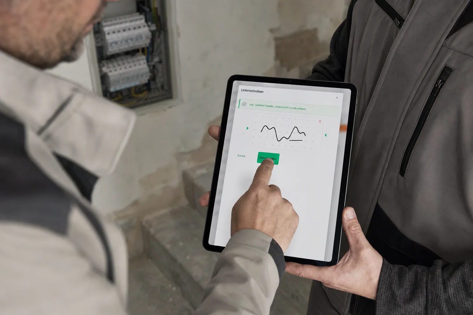 Bauleiter unterschreibt den Regiebericht des Elektrikers am iPad, im Hintergrund der neue Unterverteiler