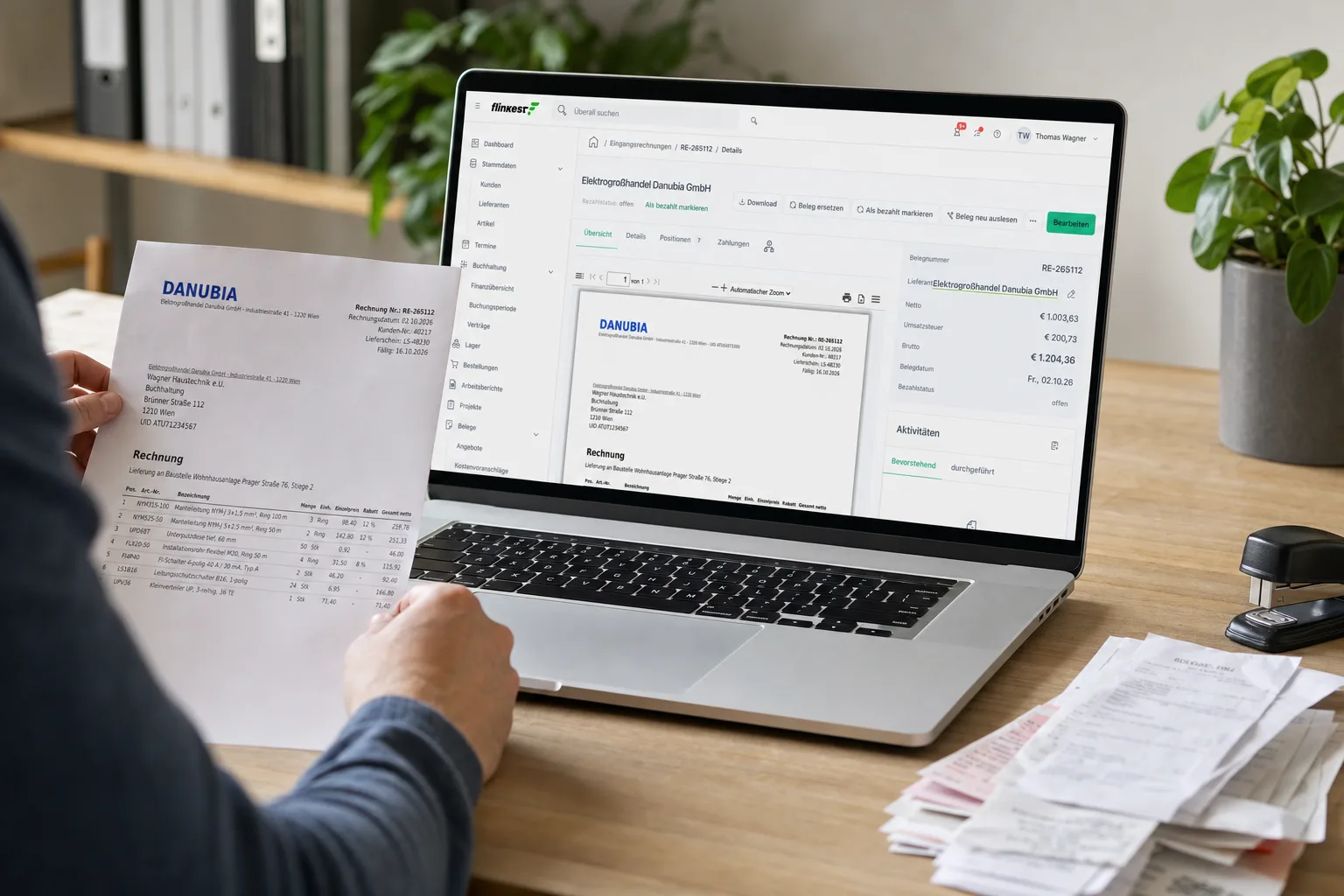 Papierrechnung des Elektrogroßhändlers in der Hand, daneben am Laptop dieselbe Rechnung von der KI ausgelesen