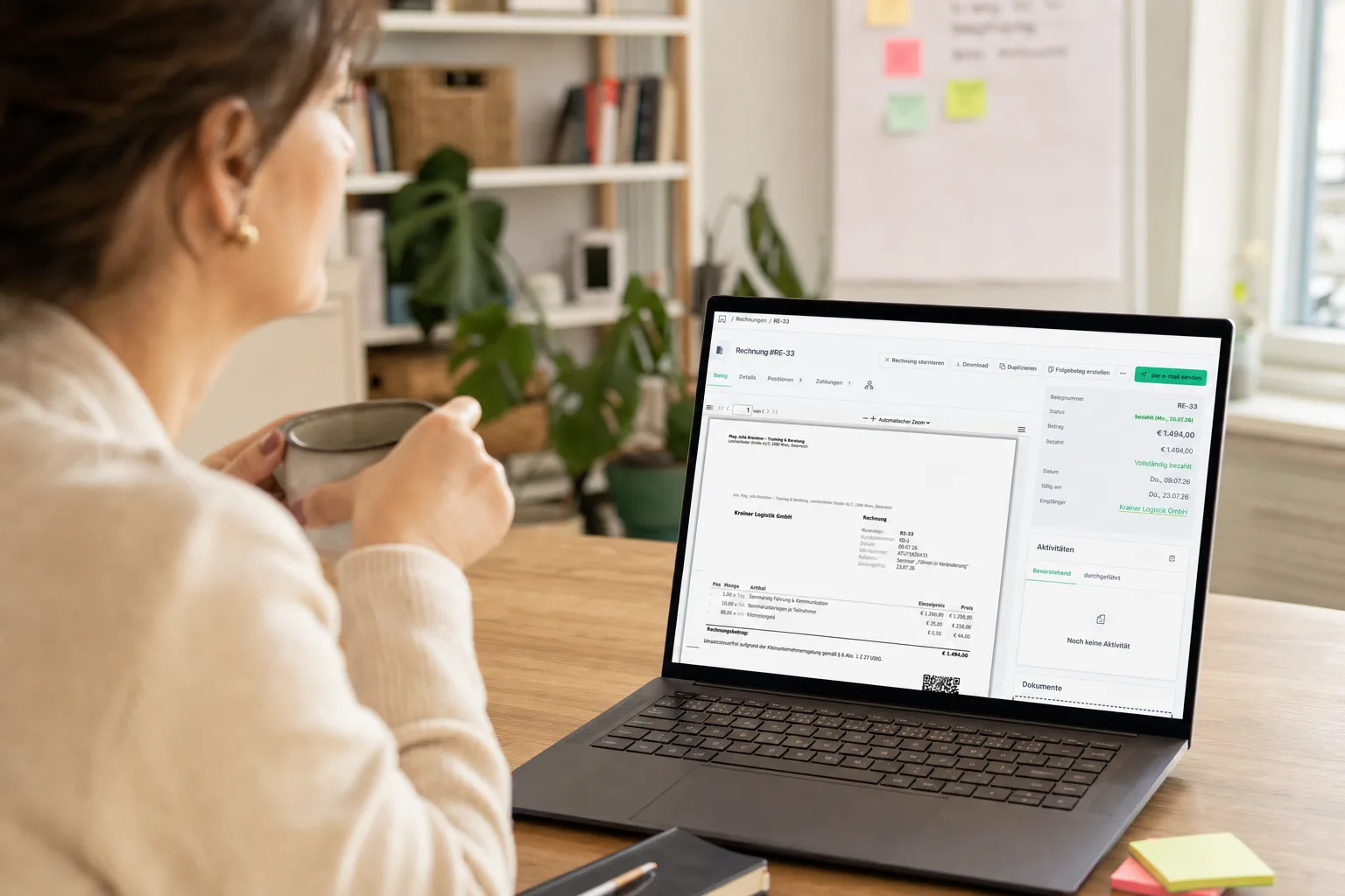 Selbstständige Trainerin mit Kaffeetasse am Schreibtisch, auf dem Laptop eine bezahlte Rechnung ohne Umsatzsteuer mit dem Hinweis zur Kleinunternehmerregelung