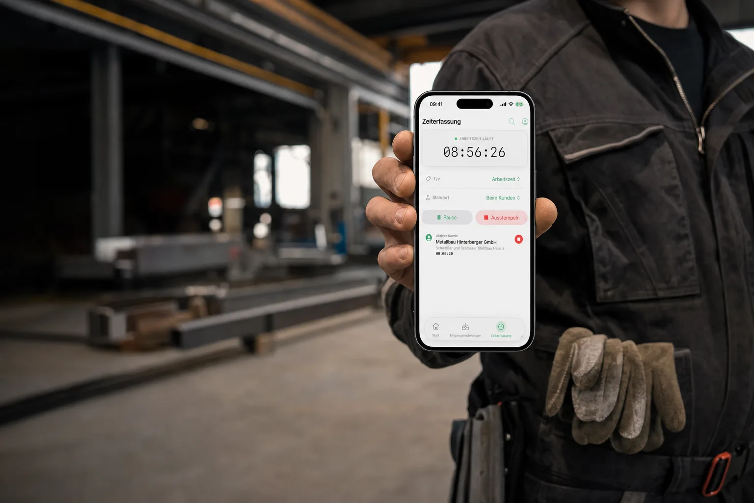 Überlassener Schweißer in der Halle des Einsatzbetriebs zeigt das Handy: Arbeitszeit läuft, Standort beim Kunden, aktiver Kunde Metallbau Hinterberger