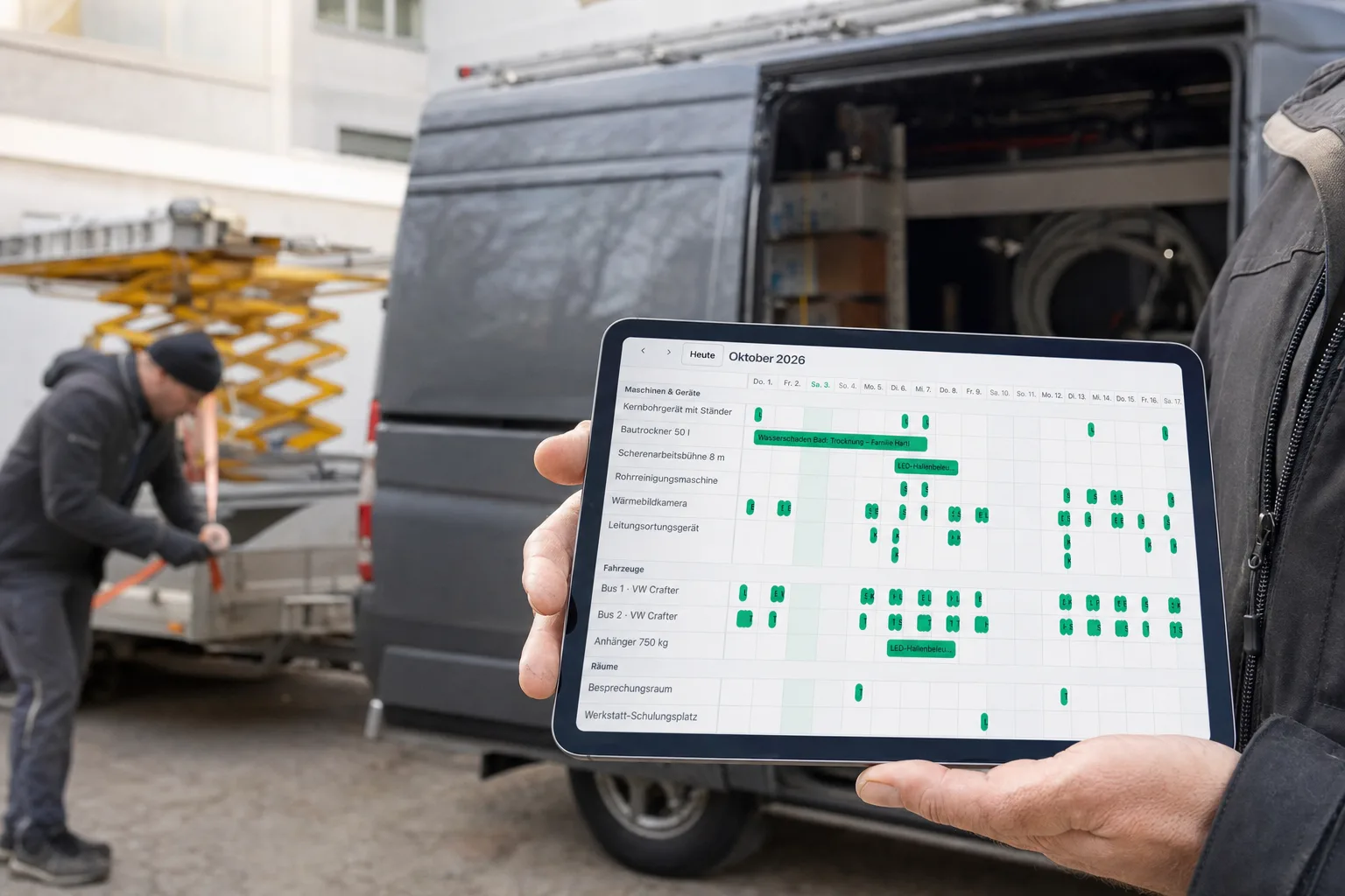Inhaber hält im Firmenhof ein Tablet mit der Ressourcen-Zeitleiste, dahinter wird eine Arbeitsbühne auf den Anhänger geladen